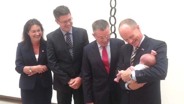 Premier Campbell Newman holds Alice, the newborn daughter of his chief of staff, Ben Myer, while Ian Walker (second from right), his ministerial appointment, looks on.