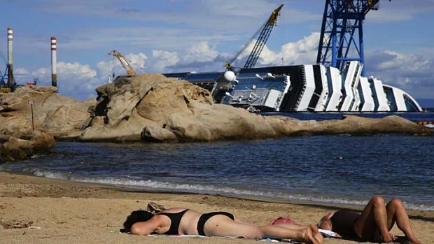 People sunbathe near the capsized cruise liner Costa Concordia near the harbour of Giglio Porto.