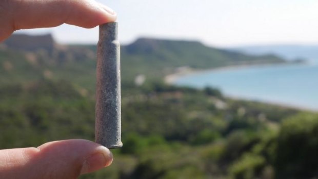 A member of the archaeologist team displays a battlefield find – with Anzac Cove in the background.