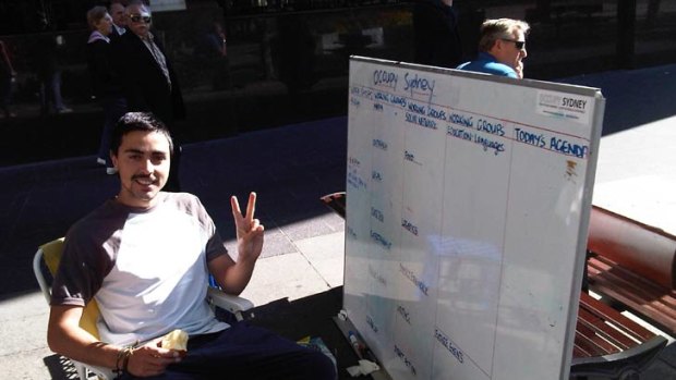 Antu Vilches-Cabrera sits beside a noticeboard listing the talks held at the protest site.