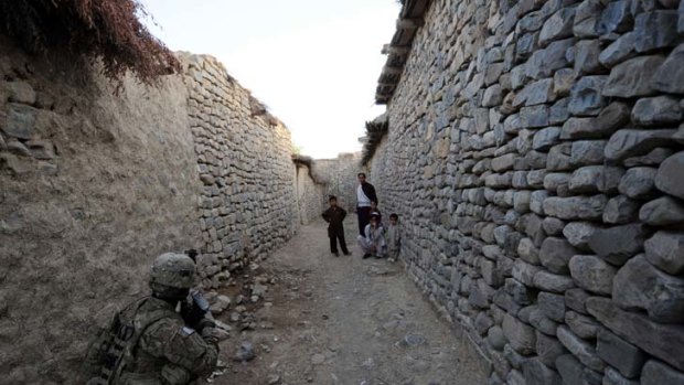 A US soldier takes a position in an alley during a house-to-house search in a village in Afghanistan's Khost province as children gather to watch.