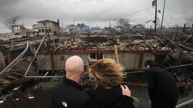 A couple survey the remains of the burnt-out home owned by her parents in Breezy Point, New York.