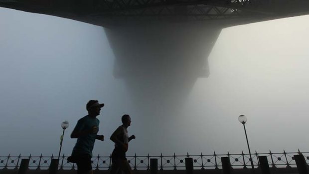 Cloaked-in morning: Joggers run below the Harbour Bridge as fog shrouds the city early on Sunday.