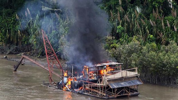 An illegal gold dredge burns on a river near the Amazon city of Puerto Maldonado, as officials crack down on rainforest destruction.