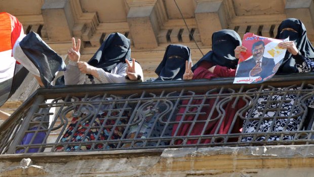 Fully-veiled Muslim women who support Egypt's deposed president Mohamed Mursi wave a national flag from the balcony of an apartment overlooking a  al-Nasr street in Cairo where a demonstration against the acting government was held .
