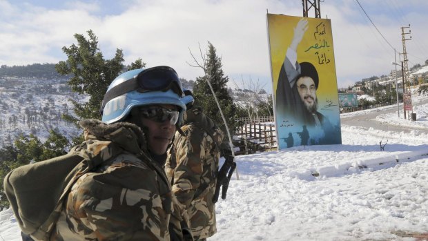 UN peacekeepers in Lebanon stand next to a banner for Lebanon's Hezbollah leader Hassan Nasrallah in snow-covered Kfar Kila village near the Lebanese-Israeli border.