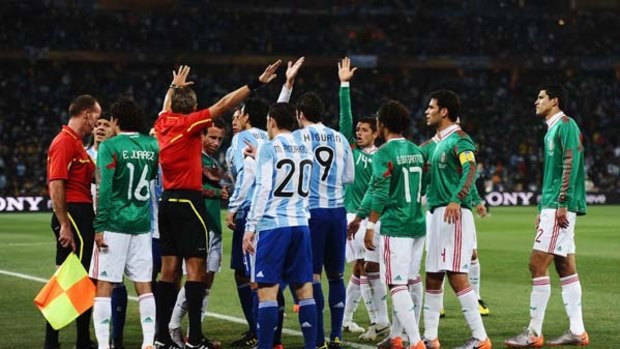 Referee Roberto Rosetti urges players away from  referee's assistant Stefano Ayroldi over the controversial Carlos Tevez goal against Mexico.