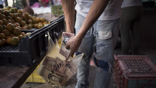 A fruit seller keeps 100-bolivar notes in a grocery bag at a fruit stand in Caracas on Monday.