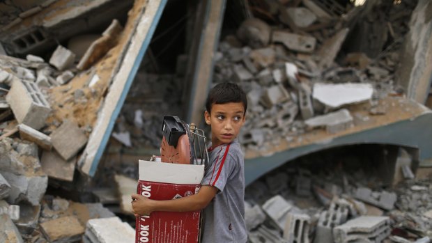 A Palestinian boy carries belongings as he walks past a house which police said was destroyed in an Israeli air strike, in Gaza City.