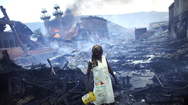 A woman picks her way through debris in central Port-au-Prince as an iron market built in 1889 burns nearby.