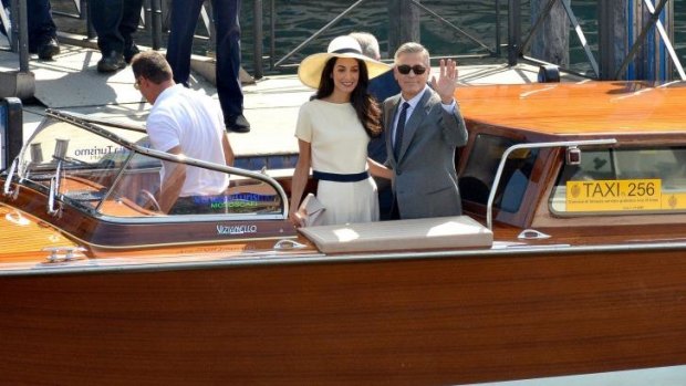 George Clooney, flanked by his wife Amal Alamuddin, waves from a water-taxi after leaving the city hall in Venice, Italy.