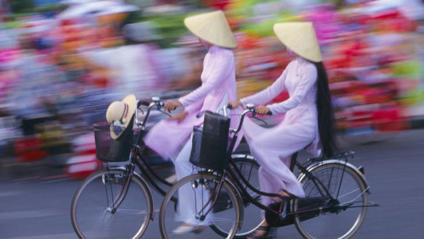Two women dressed in traditional ao dai costume riding bicycles in Ho Chi Minh City.