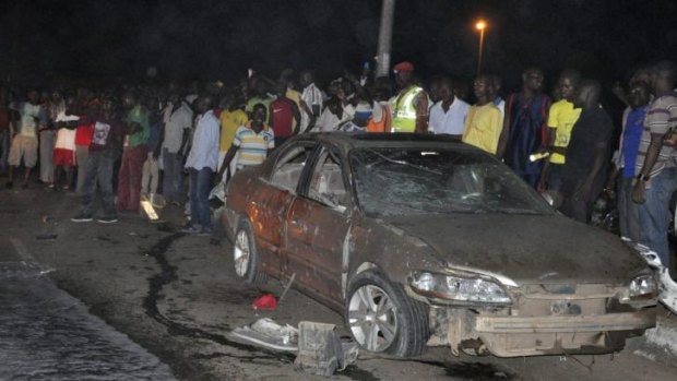 People gather near a damaged car following the bomb explosion that killed at least 18 people.
