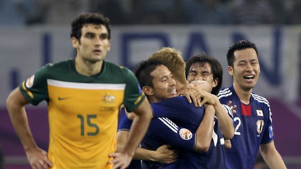 Japan players celebrate the winning goal as Australian midfielder Mile Jedinak ponders what might have been for the Socceroos.