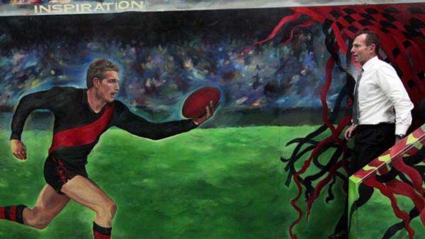 Tony Abbott walks past a mural featuring James Hird during a visit to the Essendon Football Club.