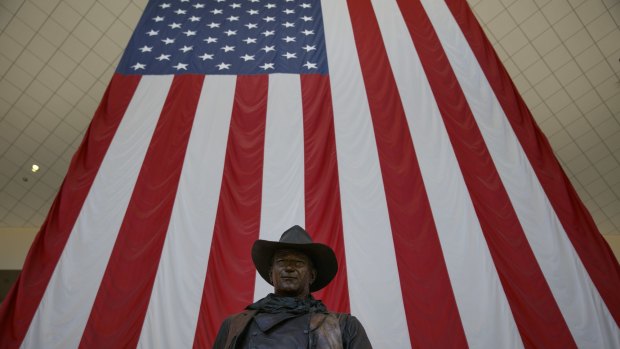 A John Wayne statue stands beneath an American flag at John Wayne Airport.