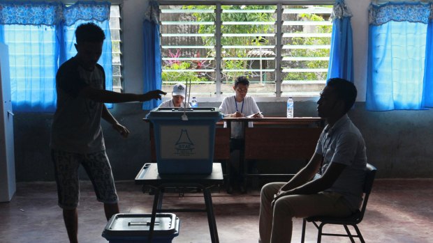 A man casts his ballot as an electoral worker, left, looks on during the presidential election at a polling station in Dili, East Timor.