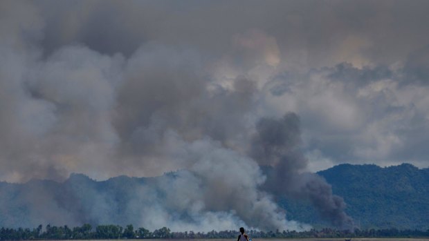 A Bangladeshi boy walks towards a parked boat as smoke rises from across the border in Myanmar, at Shah Porir Dwip, Bangladesh. 