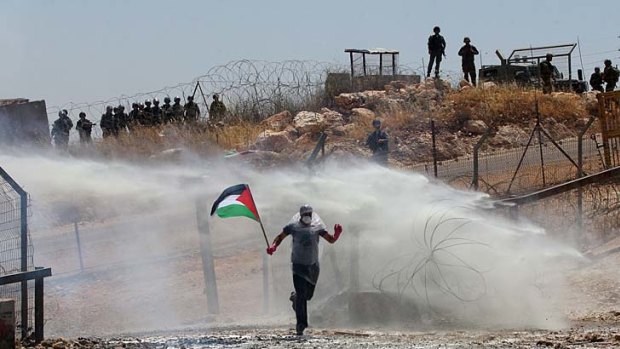 A protestor holding the Palestinian national flag runs amidst tear gas smoke fired by Israeli forces.