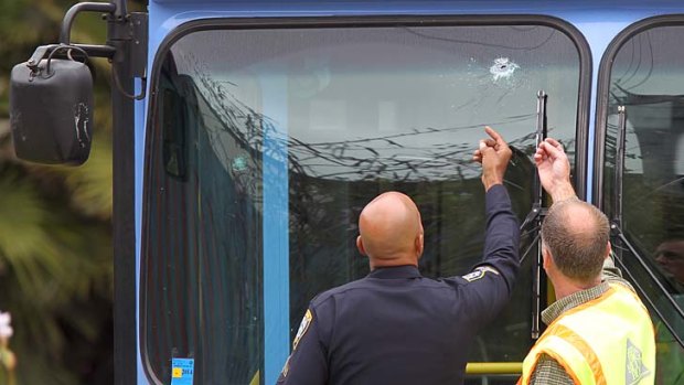 A police officer and a transit official look at a bullet hole, one of many, in a public transit bus in which two passengers were shot.