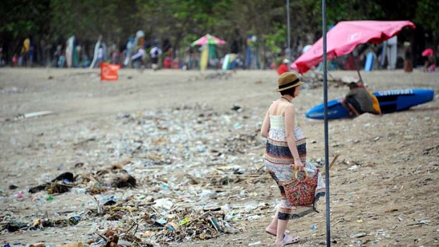 A foreign tourist walks past debris and rubbish washed ashore by the tide along Kuta beach in Bali.