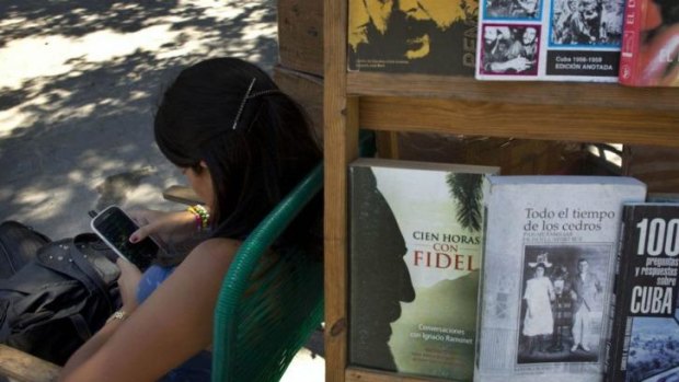 A book street vendor passes the time on her smart phone as she waits for customers in Havana, Cuba.