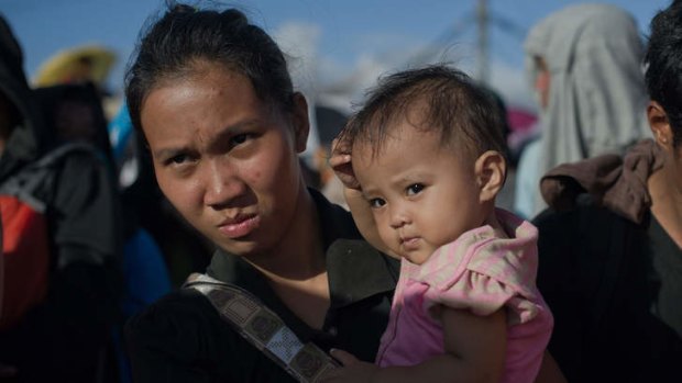 A typhoon victim holds her baby as they wait for an opportunity to board an army plane to leave the disaster zone area.