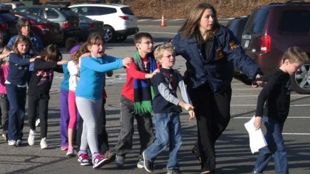 In this photo provided by the Newtown Bee, police lead children from the Sandy Hook Elementary School after the shooting.