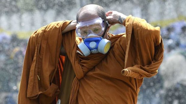 A Buddhist monk puts on a gas mask as riot police use water cannon and tear gas against anti-government protesters outside Government House in Bangkok.