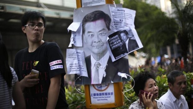 Pro-democracy supporters rest in the streets where a defaced picture of Hong Kong's Chief Executive Leung Chun-ying is plastered on a sign post.