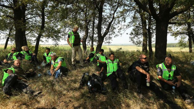 Dutch and Malaysian police take shelter from the sun as they await news on the outskirts of Rassypnoye near the crash site.