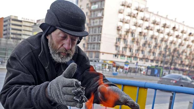 A homeless man warms up near an outside coal fire on a street in Warsaw as temperatures dropped.