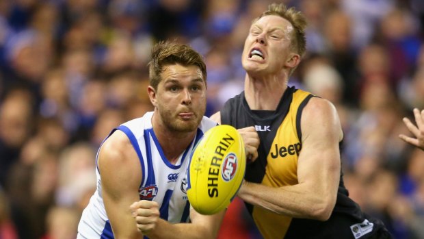 Brad McKenzie of the Kangaroos handballs as he is tackled by Jack Riewoldt of the Tigers.