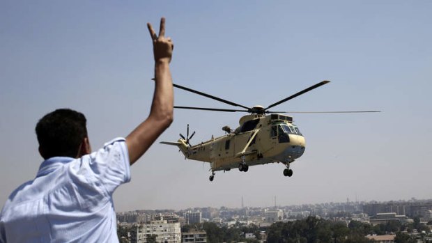 Strong presence: A man flashes a victory sign at an Egyptian military helicopter as it flies over the presidential palace in Cairo.