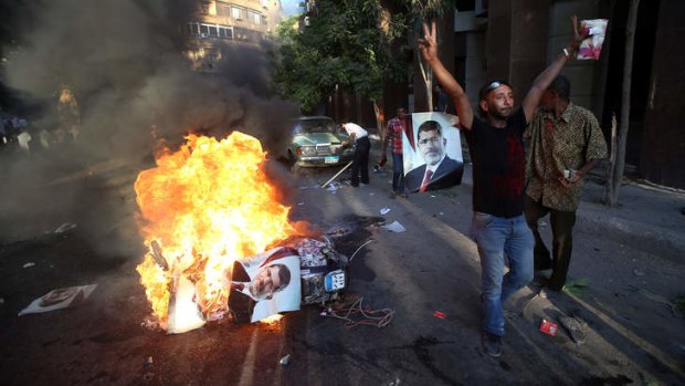 An opponent of ousted President Mohammed Mursi flashes the victory sign next to a burning scooter and posters of the former leader.