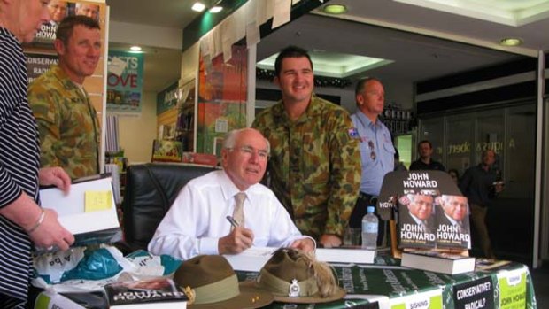 Former Prime Minister John Howard signs copies of his autobiography for two Australian soldiers during a promotional event in Brisbane.