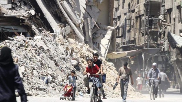 Boys ride a bicycle past other civilians near damaged buildings in Damascus.