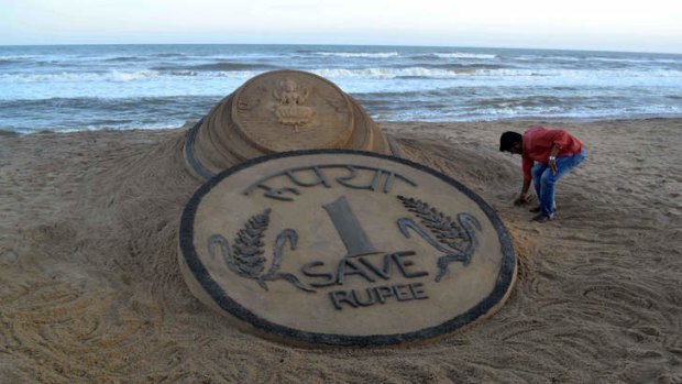 Indian sand artist Sudarsan Pattnaik puts the finishing touches to his sand sculpture of a coin. In just three months, India’s currency has fallen 14 per cent against the US dollar.