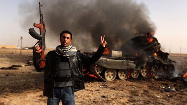 A Libyan rebel gives the sign for victory in front of a burning loyalist tank in the town of Ajdabiya.