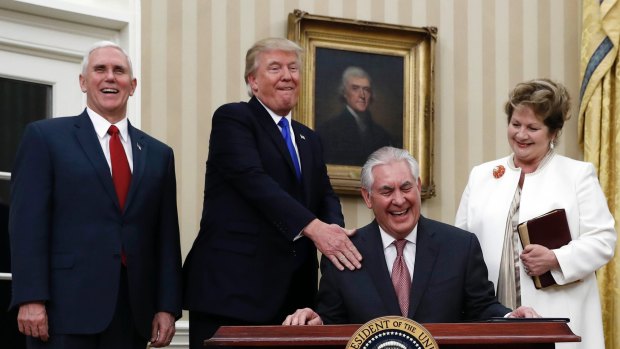 US Secretary of State Rex Tillerson (seated), joined by President Donald Trump, Vice-President Mike Pence (left) and his wife Renda St. Clair, laughs after  being sworn in. 