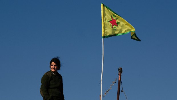 A YPG fighter stands atop a farmhouse near the contested town of Tel Hamis, the yellow YPG flag raised to symbolise the area's liberation from IS. 