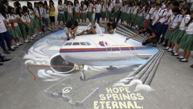 A world waits in hope ... Students watch as a group of artists put the finishing touches to a three dimensional artwork, based on the missing Malaysia Airlines flight MH370, that was painted on a school ground in Makati city, metro Manila.