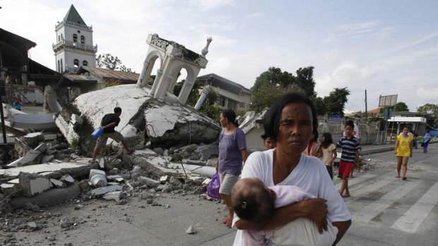 A woman carries her baby past a destroyed church on the island of Bohol on Wednesday.