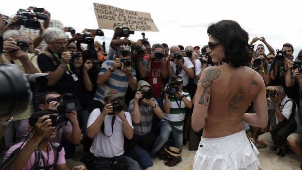 Media members surround a woman as she takes off her top at a protest, at Ipanema beach.