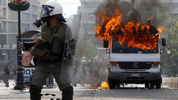 Riot policemen defend their position beside a burning van during violent protests against austerity measures in Athens