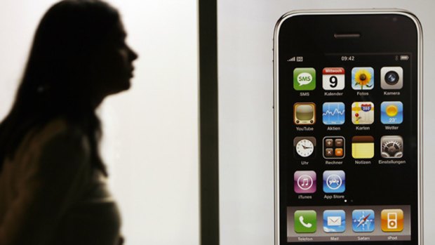 A woman is silhouetted as she walks past an iphone display.