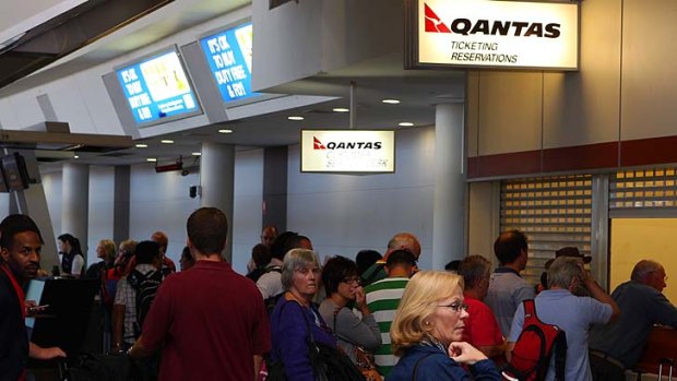 Passengers queue to talk with Qantas customer service staff.