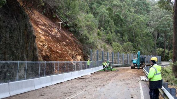 Race to reopen ... workers fix fencing following the landslide on the Kings Highway.