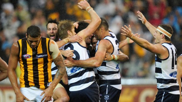Over and out: Lance Franklin, bowed and beaten, leaves the scene of the Hawks' agony as Geelong players celebrate a two-point win at the MCG yesterday.