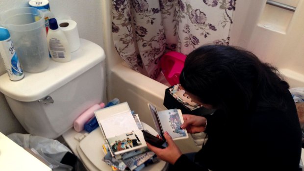 A woman straddles the toilet and rifles through photo albums.